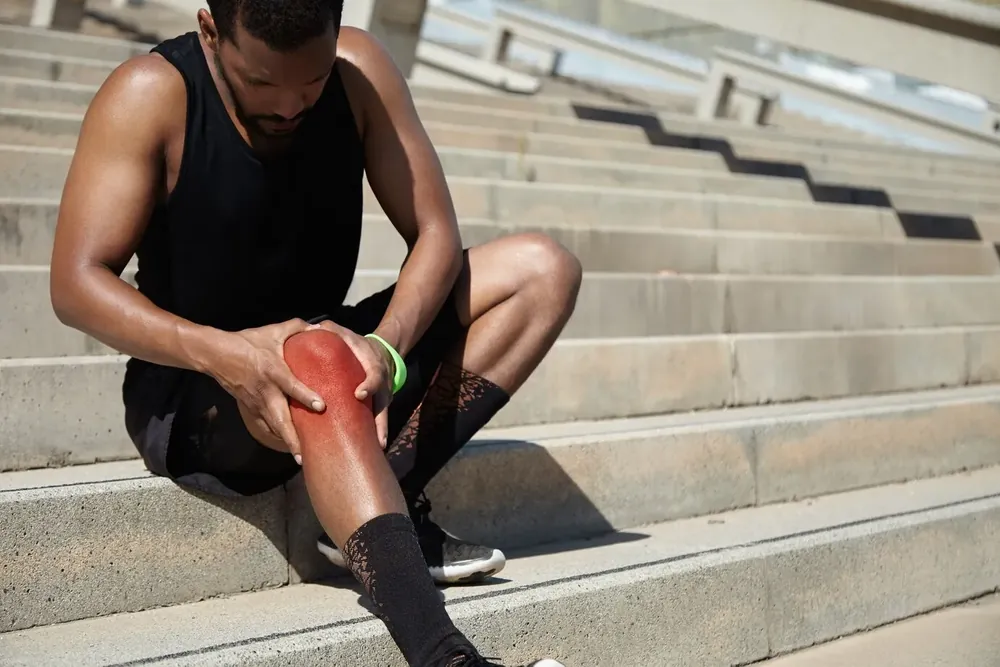 Man sitting on stadium steps holding a painful knee
